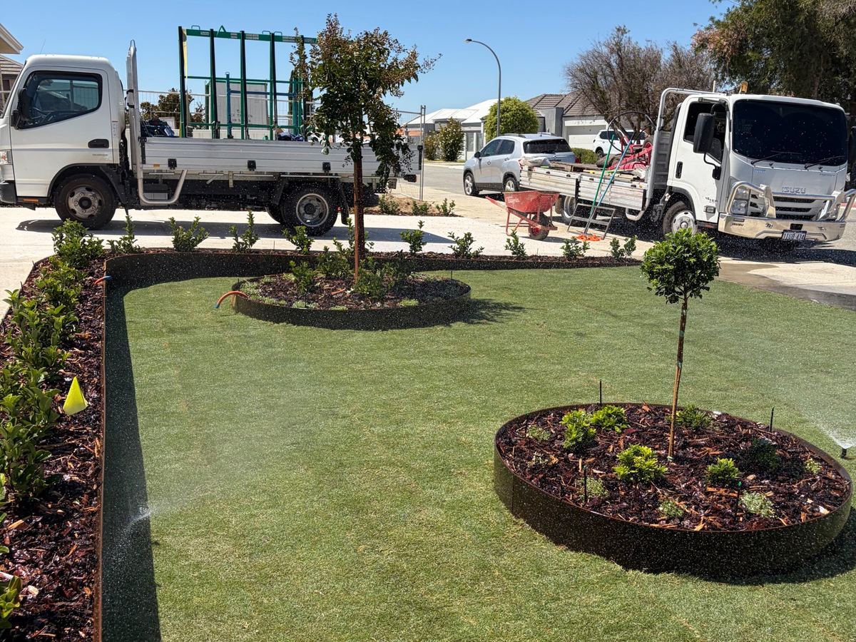Front lawn with Corten tree rings and running sprinklers